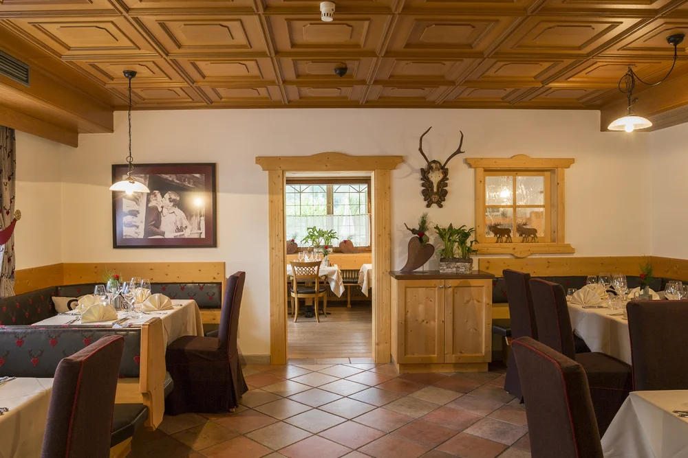 Another view of the historic Alphotel Tyrol dining room: warm wood tones, cosy alcove seating and an open passage to the adjoining room convey the house's grounded, familial atmosphere.