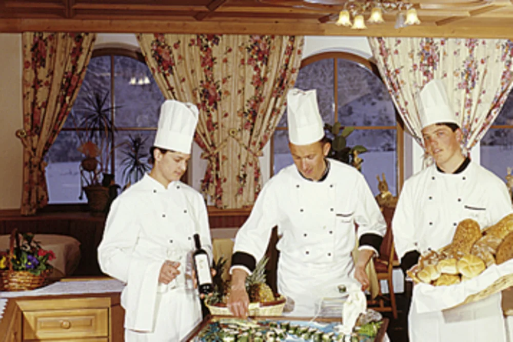 The Alphotel Tyrol kitchen team at work: three chefs proudly present fresh bread and a carefully arranged dish.