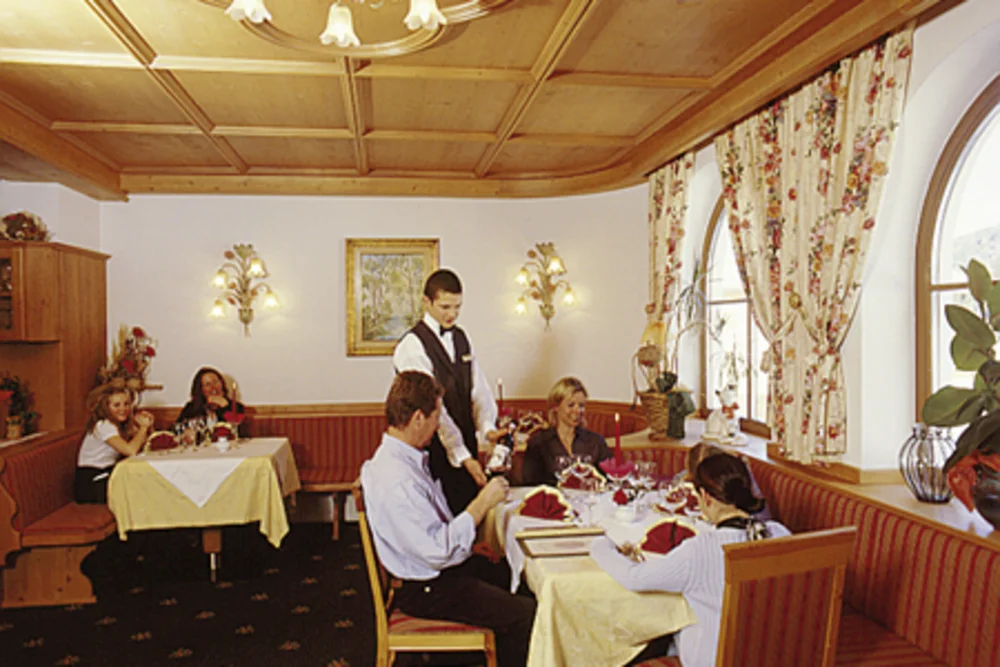 Attentive restaurant service at the Alphotel Tyrol: a waiter looks after guests in a cosy atmosphere, surrounded by warm wood and floral decor.