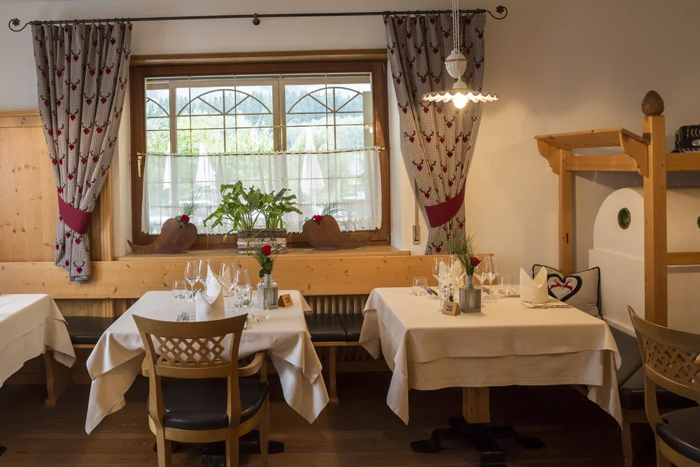 The traditional stube of the Alphotel Tyrol, warm in wood tones, with patterned curtains and a tiled stove — a room that speaks to the house's farming origins.