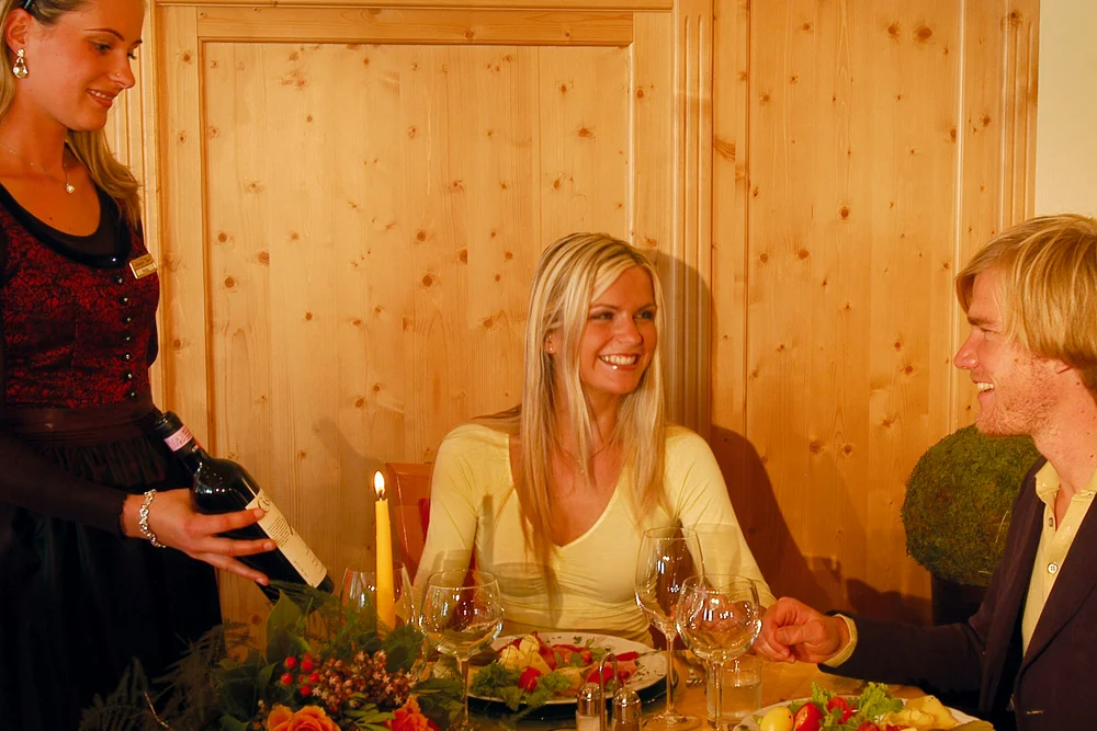 Attentive service at the Alphotel Tyrol: a staff member in traditional dress pours wine for a couple of guests by candlelight during dinner.