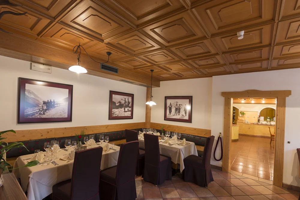 A look into the historic dining room of the Alphotel Tyrol: rustic wood-panelled ceiling, festively set tables and photographs of early ski pioneers speak to the house's long tradition.