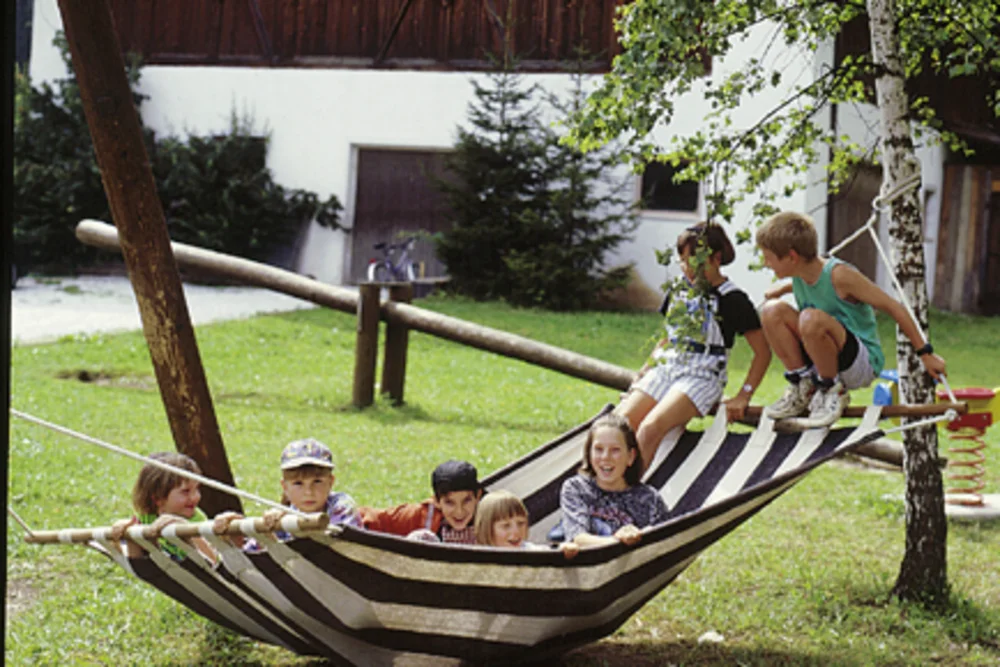 Carefree play at the Alphotel Tyrol: a group of children crowd happily onto the garden hammock — an image of childhood lived outdoors.