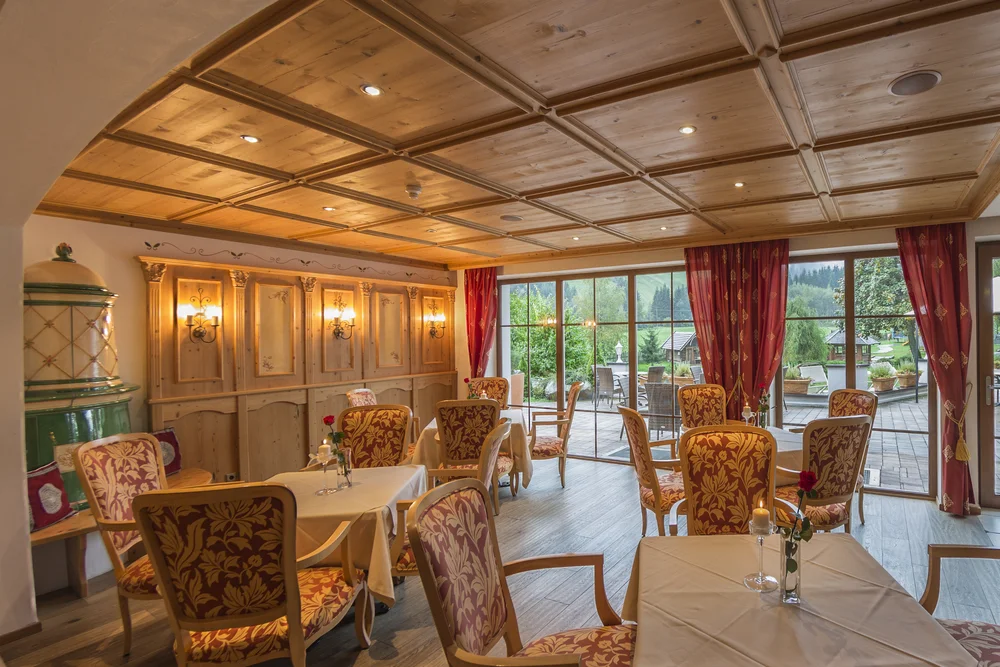 A look into the traditional stube of the Alphotel Tyrol: warm wood, festive upholstered furniture and a historic tiled stove create an inviting atmosphere with direct terrace access.